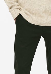 Gebreide trui in roomkleur met een ronde hals, gecombineerd met donkergroene, slim-fit broek. De stof oogt glad met een subtiele glans.