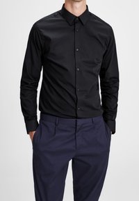 Zwart overhemd met lange mouwen en knoopsluiting, voorzien van een puntige kraag, met een gladde textuur en een aansluitend ontwerp, gecombineerd met marineblauwe broek.