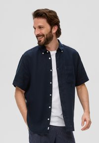 Marineblauwe korte mouwen knoopshirt in een relaxte pasvorm, met een opgestikt zakje, witte knopen en een gladde structuur over een wit t-shirt.