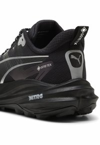 Czarny but do biegania z materiałem Gore-Tex, wyściełanym kołnierzem, teksturowaną powierzchnią, refleksyjnymi srebrnymi akcentami i charakterystyczną formowaną czarną podeszwą.