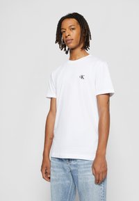 T-shirt bianca in cotone con maniche corte, caratterizzata da un piccolo logo CK nero sul lato sinistro del petto. La vestibilità è casual e dritta.