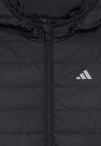 Giacca a vento nera con zip frontale e cappuccio, con texture trapuntata e logo riflettente sul lato sinistro.