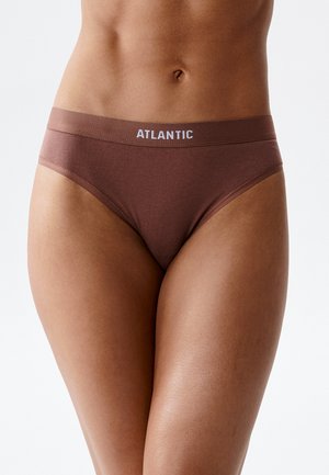 Zbliżenie tułowia w brązowych majtkach z wysokim stanem z napisem „ATLANTIC” na pasie na jednolitym tle.