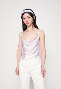 Camisola de cetim lavanda com frente drapeada, alças finas e silhueta ajustada, combinada com calças brancas de cintura alta.