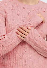 Maglione lavorato a maglia rosa chiaro con un motivo testurizzato, dettagli a giorno, polsini a coste e scollatura rotonda.