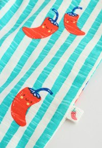 Modrobiely pruhovaná textília s červenými chilli papričkami, ktoré majú usmievavé tváre a modré stonky.