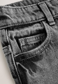 Primer plano del bolsillo de unos vaqueros vaqueros en blanco y negro con costuras visibles, trabilla para cinturón y remache metálico sobre tela texturizada.