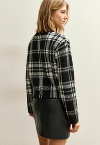 Czarny i biały sweter w kratkę o skróconym kroju, pleciona tekstura, z długimi rękawami, zestawiony z czarną skórzaną mini spódnicą.