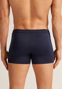 Bañador azul marino con textura suave y cintura elástica, con un diseño ajustado que llega a la mitad del muslo, sin marcas visibles.