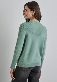 Grüner Strickpullover mit einem gerippten Rücken- und Schulterdesign. Der Stoff wirkt weich und hat einen lässigen Schnitt mit langen Ärmeln.