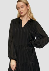 Robe noire avec de longues manches bouffantes, un décolleté en V et une conception à volants. Le tissu présente de subtiles rayures verticales et une texture lisse.