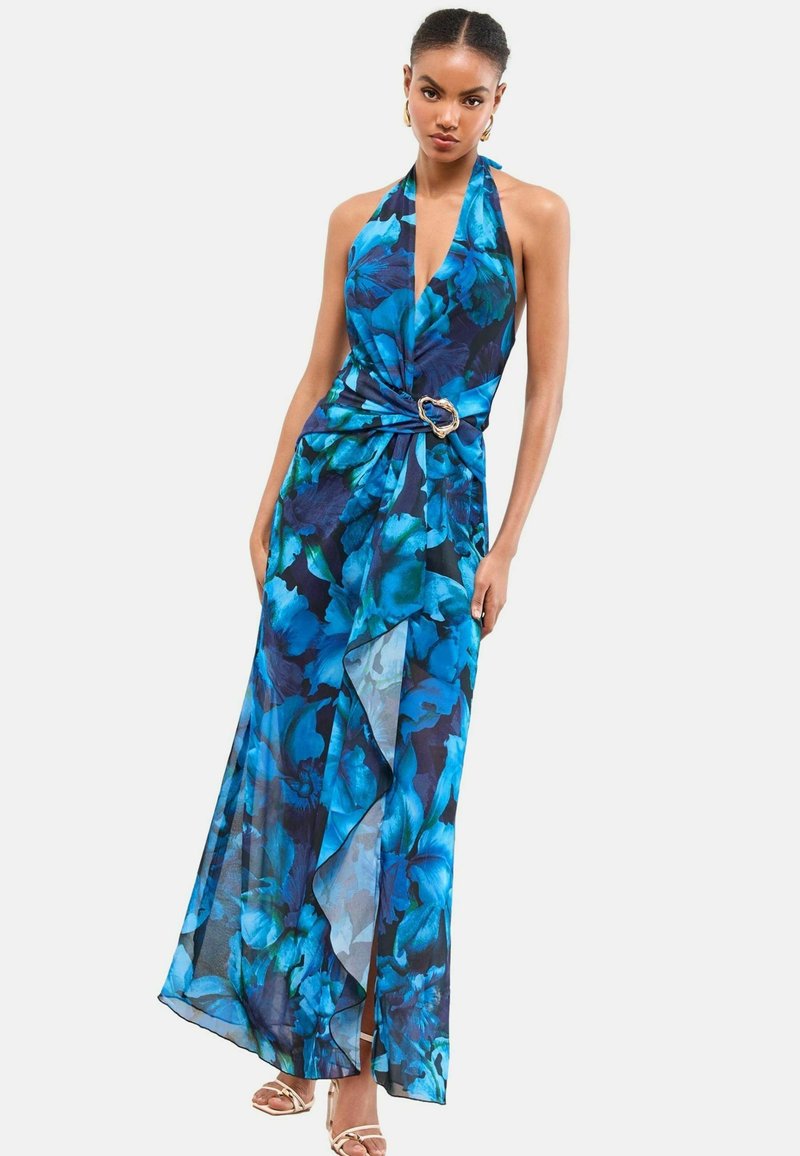 Rochie lungă, cu guler halter, prezentând un model floral albastru pe o țesătură transparentă, strânsă în talie cu un accent oval auriu.