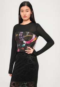 Black long-sleeve crop top with floral print panel; features a mix of sheer and opaque fabrics, highlighting textured patterns and contrasting colors.