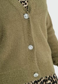 Cardigan vert olive en tissu tricoté texturé, présentant quatre grands boutons ornés et un col en V.