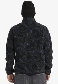 Schwarzer Fleece-Pullover mit einem gewundenen grünen und lila Muster, hohem Kragen und halbem Reißverschluss. Verfügbar mit strukturiertem Stoff und langen Ärmeln.