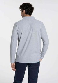 Polo shirt gris à manches longues avec col, texture subtile et fentes latérales à l'ourlet, présenté de dos.