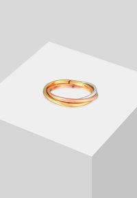 Anelli interconnessi in oro, oro rosa e argento con finiture lisce; presenta un design minimalista e una forma circolare, esposti su una piattaforma.