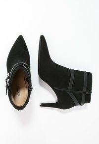 Zwarte suède enkelboots met puntige neuzen, ritssluiting en slanke zwarte bandjes. De hak heeft een metallic accent voor extra detail.