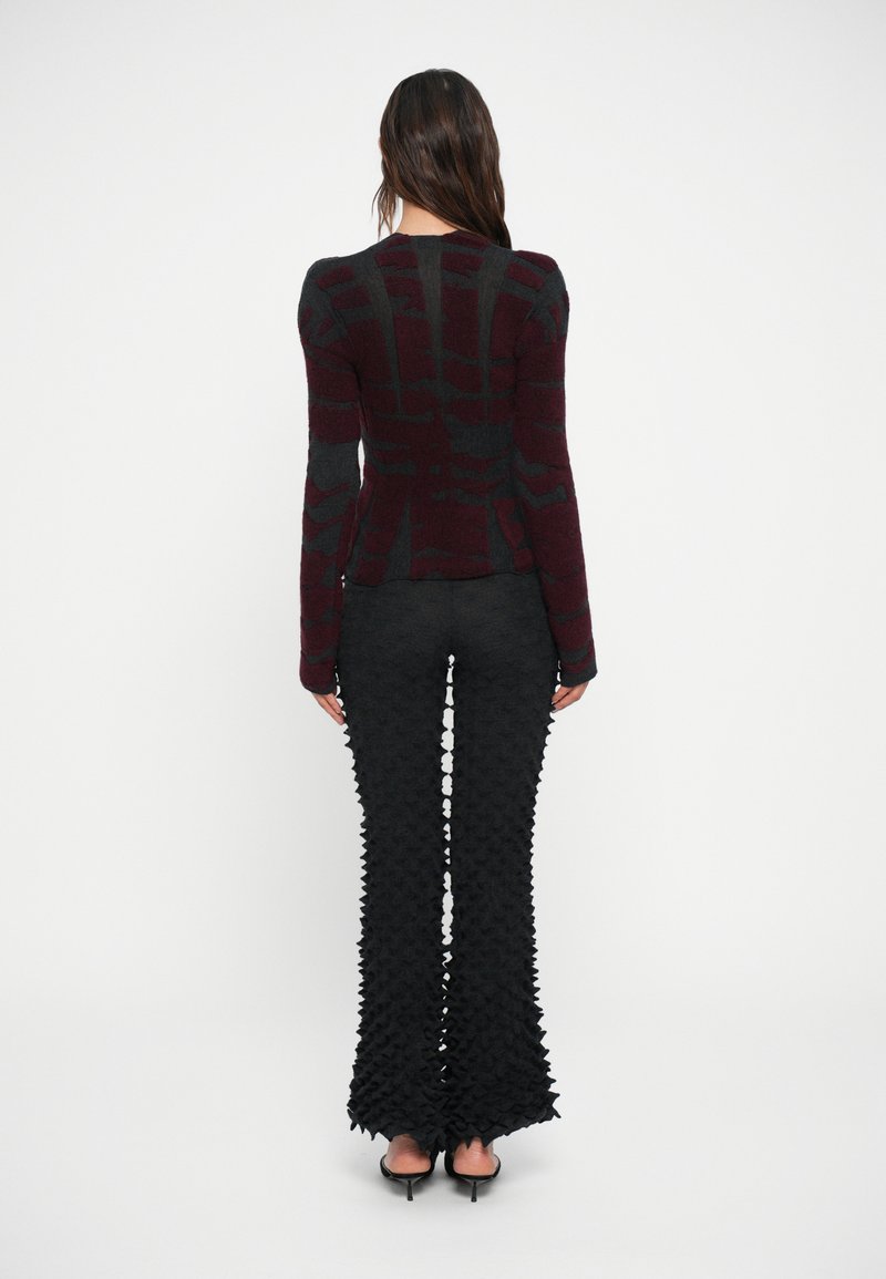 Haut à manches longues en tricot rouge et noir à motifs, associé à un pantalon évasé noir texturé avec un design tridimensionnel.