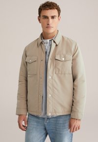Beige gewatteerde jas met drukknoopsluitingen en twee borstzakken. Draag over een lichtgrijs shirt met een gladde textuur en een casual ontwerp.