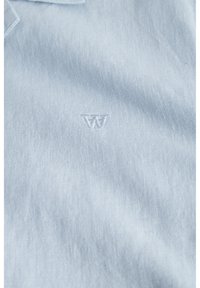Polo shirt bleu clair en tissu texturé, avec un logo brodé subtil au centre de la poitrine.