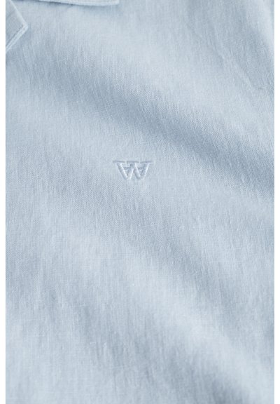 Polo shirt bleu clair en tissu texturé, avec un logo brodé subtil au centre de la poitrine.