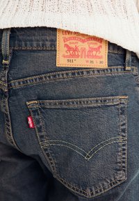 Mørkeblå denim Levi's 511 jeans med et brunt lærmerke med trykt merkevare og et rødt merke på baklommen.