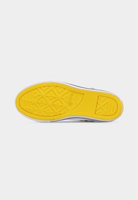 Κίτρινη λαστιχένια σόλα παπουτσιού Converse All Star με γεωμετρικά σχέδια πέλματος και λευκή μεσόσολα σε απλό φόντο.