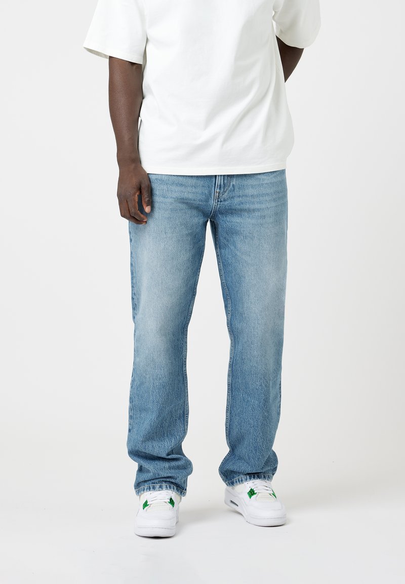 Light blue jeans made of denim with a straight-leg design, featuring subtle fading, five pockets, and worn at the cuffs. Paired with white sneakers.