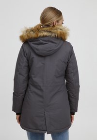 Šedá parka s kapucňou na kožušine. Má dĺžku po stehná, dlhé rukávy a rozparok vzadu pre lepšiu pohyblivosť.