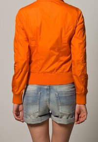 Orange zip-up bomberjacka med ribbade muddar och nederkant, parat med ljusblå denimshorts med uppvikta muddar och bakfickor.