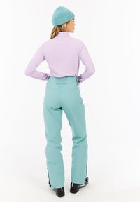 Un col roulé côtelé violet clair et un pantalon de ski teal clair avec une taille élastique, dotés de poches avant et de zippers aux chevilles.