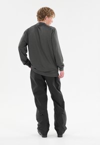 Mörkgrå långärmad skjorta med rundad fåll, i kombination med svarta byxor med sidoglidlås och avslappnad passform. Slät textur.