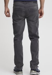 Pantalones de mezclilla gris con un diseño de pierna recta, que presentan bolsillos traseros y una textura suave. Conjunto combinado con zapatillas deportivas.