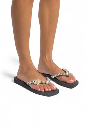 Des tongs noires avec une semelle texturée, ornées d'un accent en forme d'étoile dorée et d'embellissements en cristal sur les lanières.