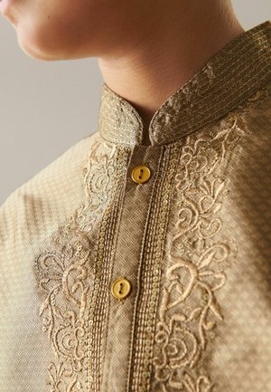 Goldfarbener Stoff mit filigraner Stickerei und einem gemusterten Stoff; verfügt über einen hohen Kragen und zwei goldene Knöpfe an der Vorderseite.