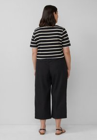 Schwarz-cream gestreiftes Kurzarmshirt mit rundem Ausschnitt, kombiniert mit lässigen schwarzen 3/4-Hosen und braunen flachen Sandalen.