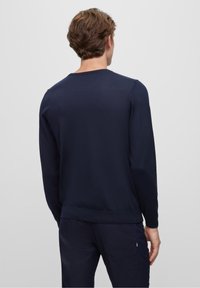 Mörkblå crew neck-tröja i texturerad tyg. Har långa ärmar och ribbad kant. Bakre vy med minimal detaljering.