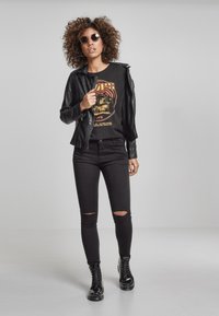 Černá kožená motorkářská bunda přes černé grafické tričko, doplněná o roztrhané černé skinny džíny a lesklé černé šněrovací boty.