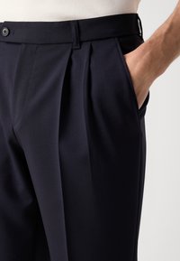 Navy pleated trousers made of soft fabric with a button closure, featuring side pockets and a tapered design.