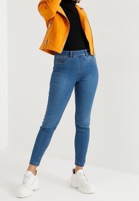 Blauwe denim skinny jeans hebben een klassiek vijf-pocket ontwerp en een slim fit, gecombineerd met een zwarte coltrui en een gele leren jas.