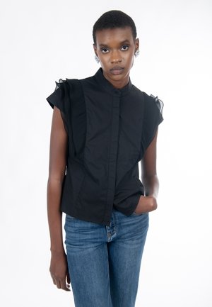 Schwarze ärmellose Bluse mit hohem Kragen, mit strukturierten Rüschen an den Schulternähten und einer Knopfleiste vorne, kombiniert mit blauer Jeans.