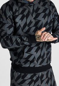 Sudadera con capucha en gris oscuro con un patrón abstracto negro, que presenta un ajuste holgado, puños acanalados y un diseño de bolsillo canguro.