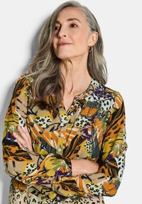 Mehrfarbige Bluse mit einem abstrakten Blumen- und Tiermuster, durchgeknöpften Vorderseite, langen Ärmeln und lockerer Passform. Hergestellt aus leichtem Stoff.