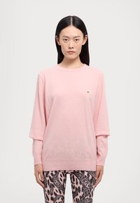 Maglione rosa chiaro realizzato in tessuto morbido, con scollo arrotondato e maniche lunghe. Un piccolo logo ricamato è visibile sul petto.