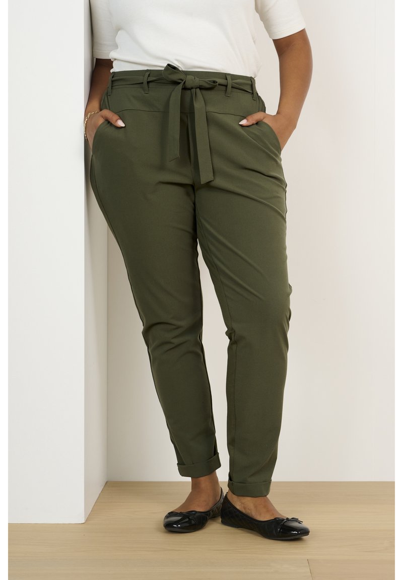 Pantaloni elasticizzati verde oliva con una vita legata, gambe affusolate, tasche laterali e orli arrotolati, abbinate a scarpe basse nere.