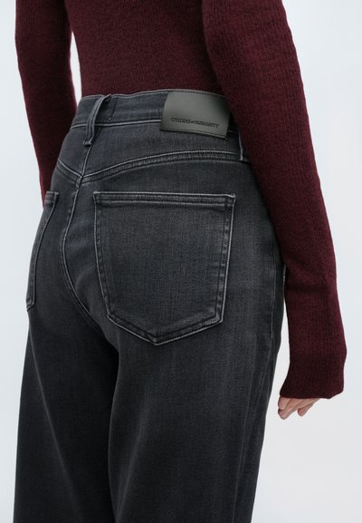 Μαύρο τζιν παντελόνι από denim με ψηλή μέση, χαρακτηριζόμενο από απαλή υφή, δύο πίσω τσέπες και δερμάτινη ετικέτα στη μέση. Το ύφασμα έχει ελαφριά γυαλάδα.