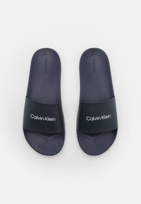 Infradito navy di Calvin Klein con una ampia fascia opaca che mostra il nome del brand in bianco. Sole in gomma morbida con una texture liscia.