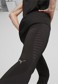 Leggings atléticos negros con un diseño texturizado que presenta un patrón en forma de chevron a lo largo del costado y un pequeño logo reflectante.