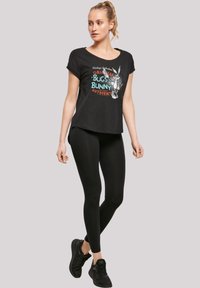 Svart t-skjorte med kort erm som har et fargerikt grafisk trykk av Bugs Bunny. Kombinert med svarte leggings og svarte joggesko.